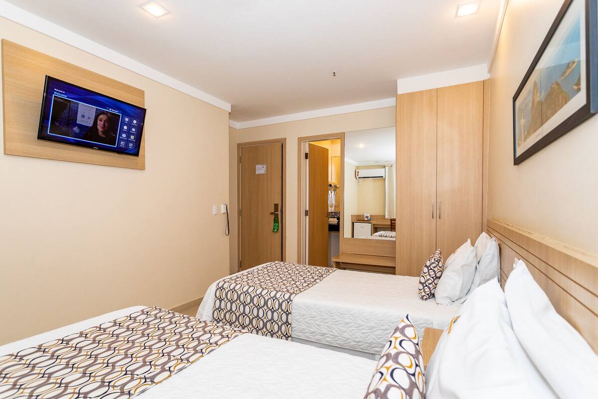 Ein Hotelzimmer mit zwei Betten, einem an der Wand befestigten Fernseher und einem Spiegel über dem Bett.
