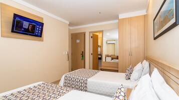 A hotel room with two beds, a TV mounted on the wall, and a mirror above the bed.