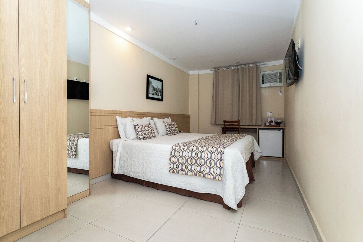 A hotel room with a bed, a desk, a TV, and a wardrobe.