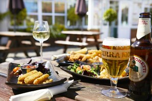 A table with a beer bottle, a glass of beer, a plate of food, and a glass of white wine.