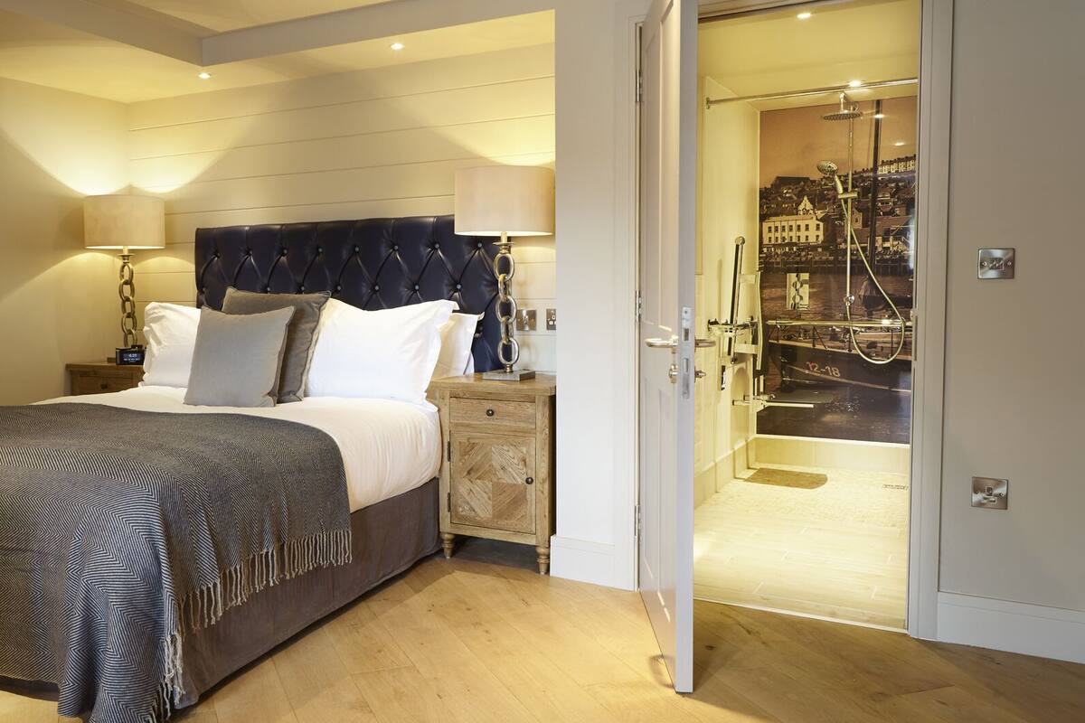 A hotel room with a bed, bedside lamps, a wooden nightstand, and a view of a cityscape through a glass door.
