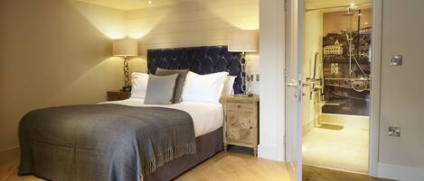 A hotel room with a bed, bedside lamps, a wooden nightstand, and a view of a cityscape through a glass door.