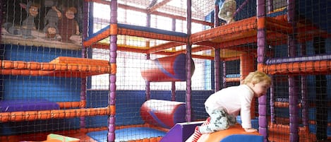 A child climbing on a play structure inside a netted play area.
