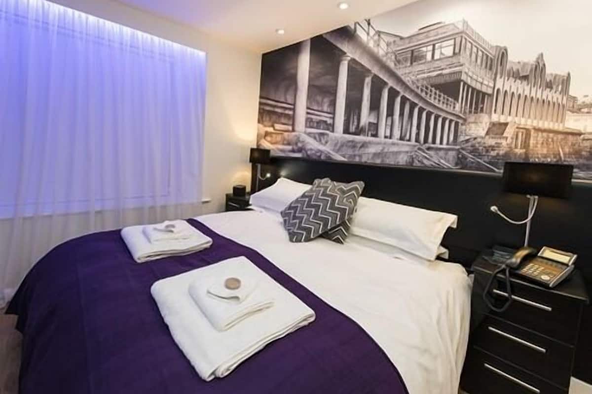 A hotel room with a bed, a nightstand, a telephone, and a wall mural.