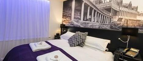 Quarto de hotel com cama, mesa de cabeceira, telefone e um mural na parede.