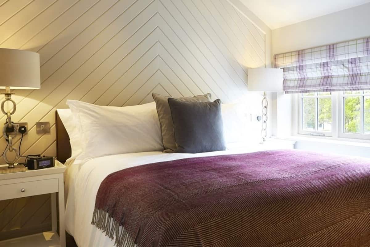 A hotel room with a bed, a nightstand, a lamp, a window with a view, and a chevron-patterned wall.