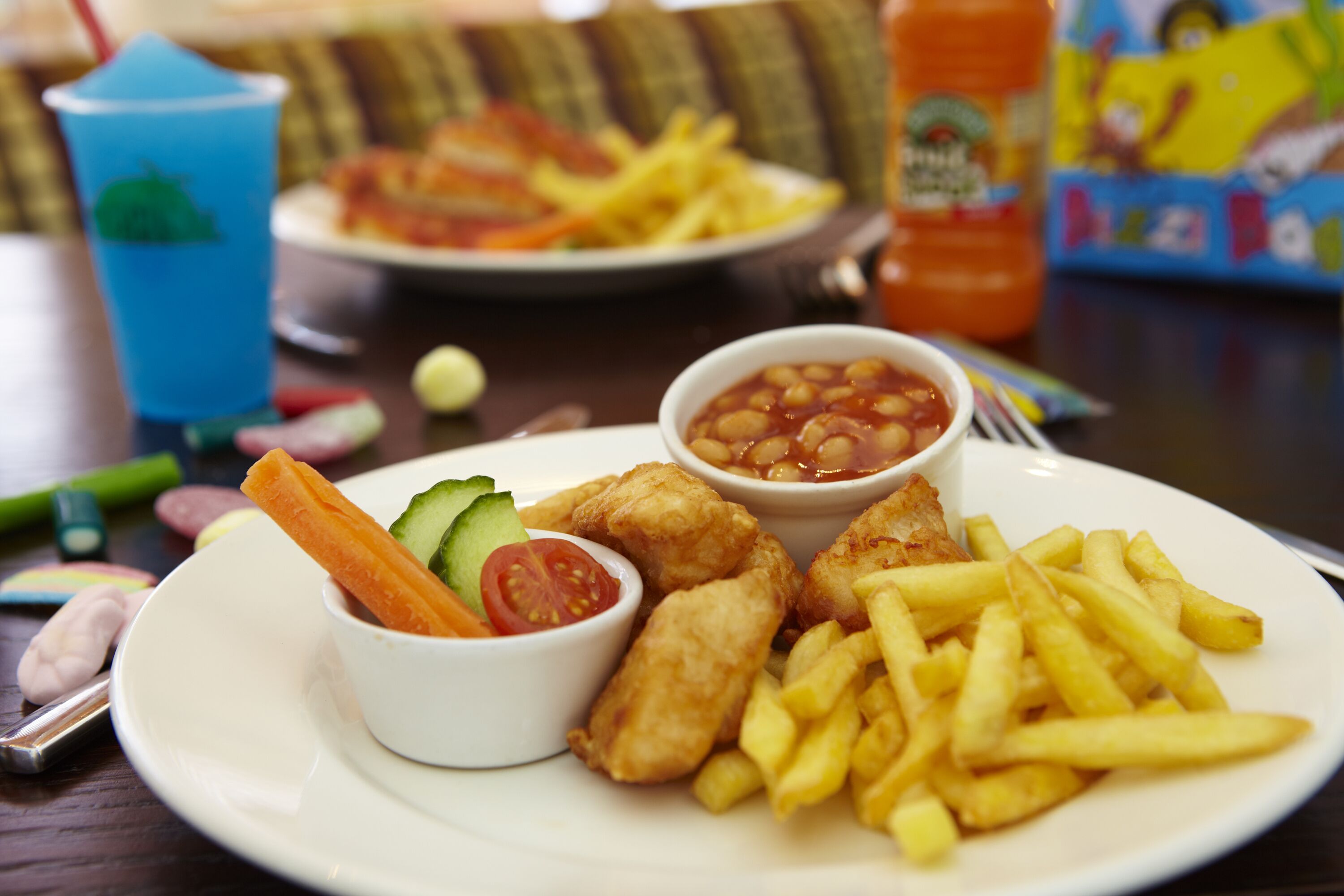Un plato de pescado con papas fritas, un bol pequeño de frijoles y una bebida.