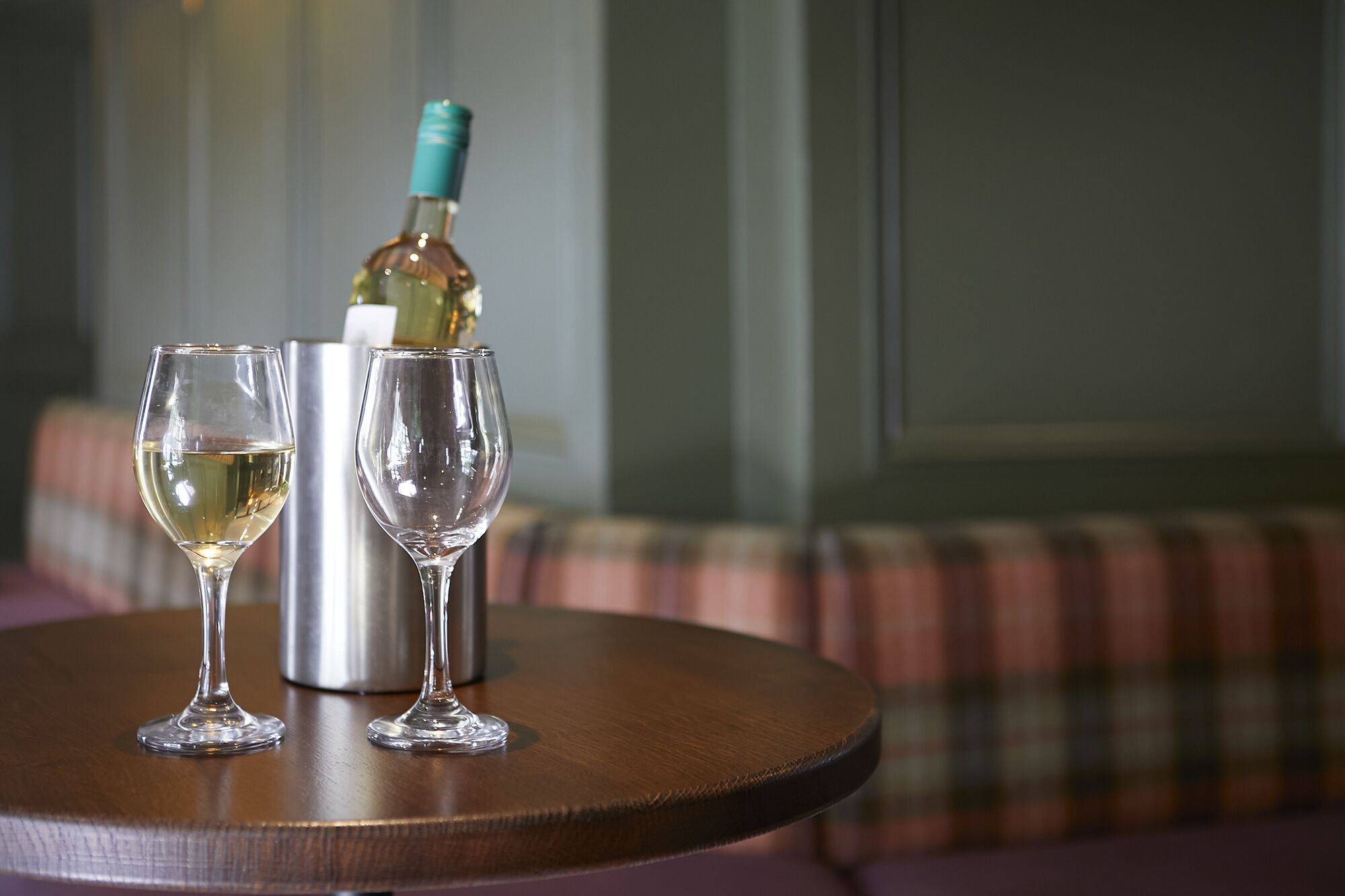 Two wine glasses on a round table with a bottle of wine in the background.