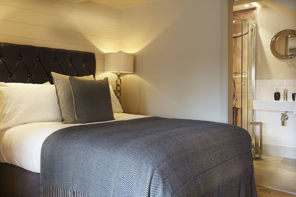 A hotel room with a bed, bedside lamps, a nightstand, a mirror, and a bathroom with a sink and shower.
