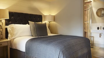 Une chambre d’hôtel comprenant un lit, des lampes de chevet, une table de nuit, un miroir et une salle de bain avec un lavabo et une douche.