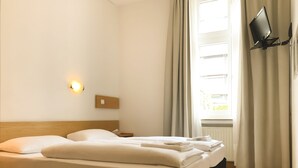 Habitación de hotel con cama, mesita de noche, televisor montado en la pared y ventana con cortinas.