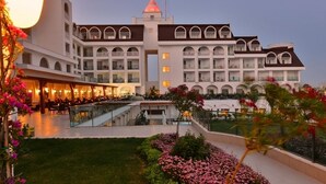 A multi-story hotel with a central courtyard, balconies, and a dining area with outdoor seating. - Side Crown Serenity Ultra All Inclusive (Manavgat)