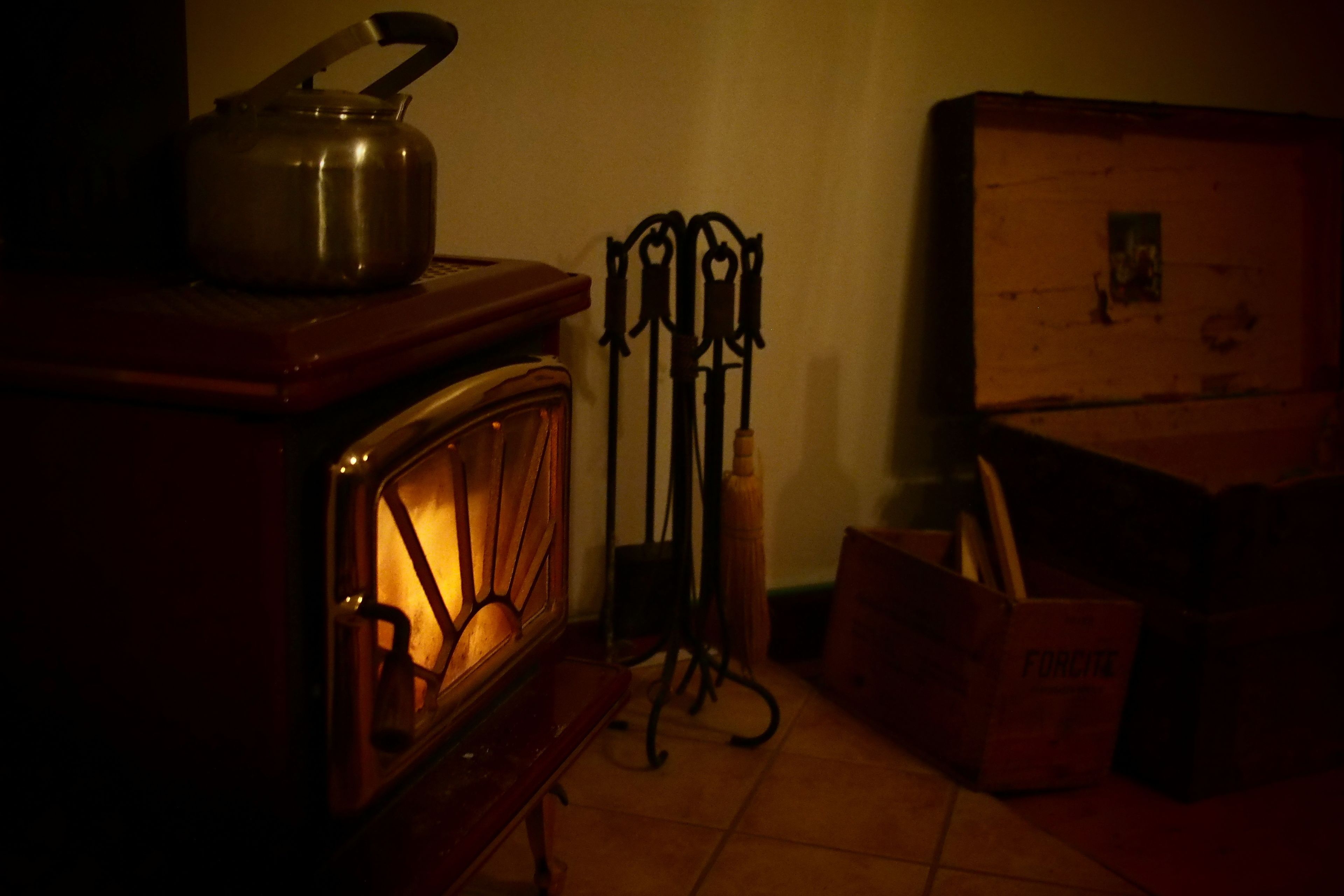 Una habitación tenuemente iluminada con un armario de madera, una tetera metálica encima y un escurridor de metal con herramientas.