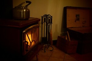 Una habitación tenuemente iluminada con un armario de madera, una tetera metálica encima y un escurridor de metal con herramientas.