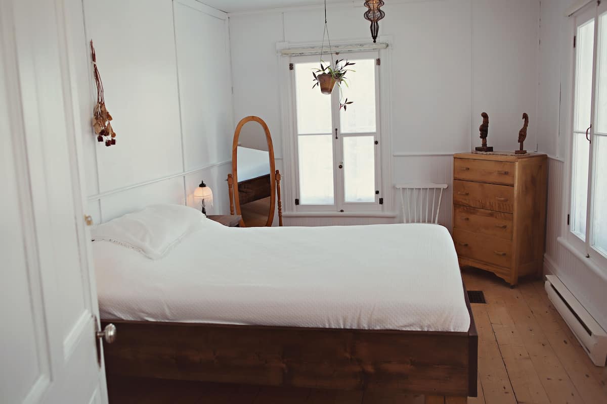 Ein Schlafzimmer mit einem hölzernen Bett, einem Schminktisch, einem Spiegel und einem Fenster mit Pflanze.