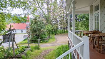 A covered porch with wooden furniture, a gravel path, and a view of a church with a red roof.