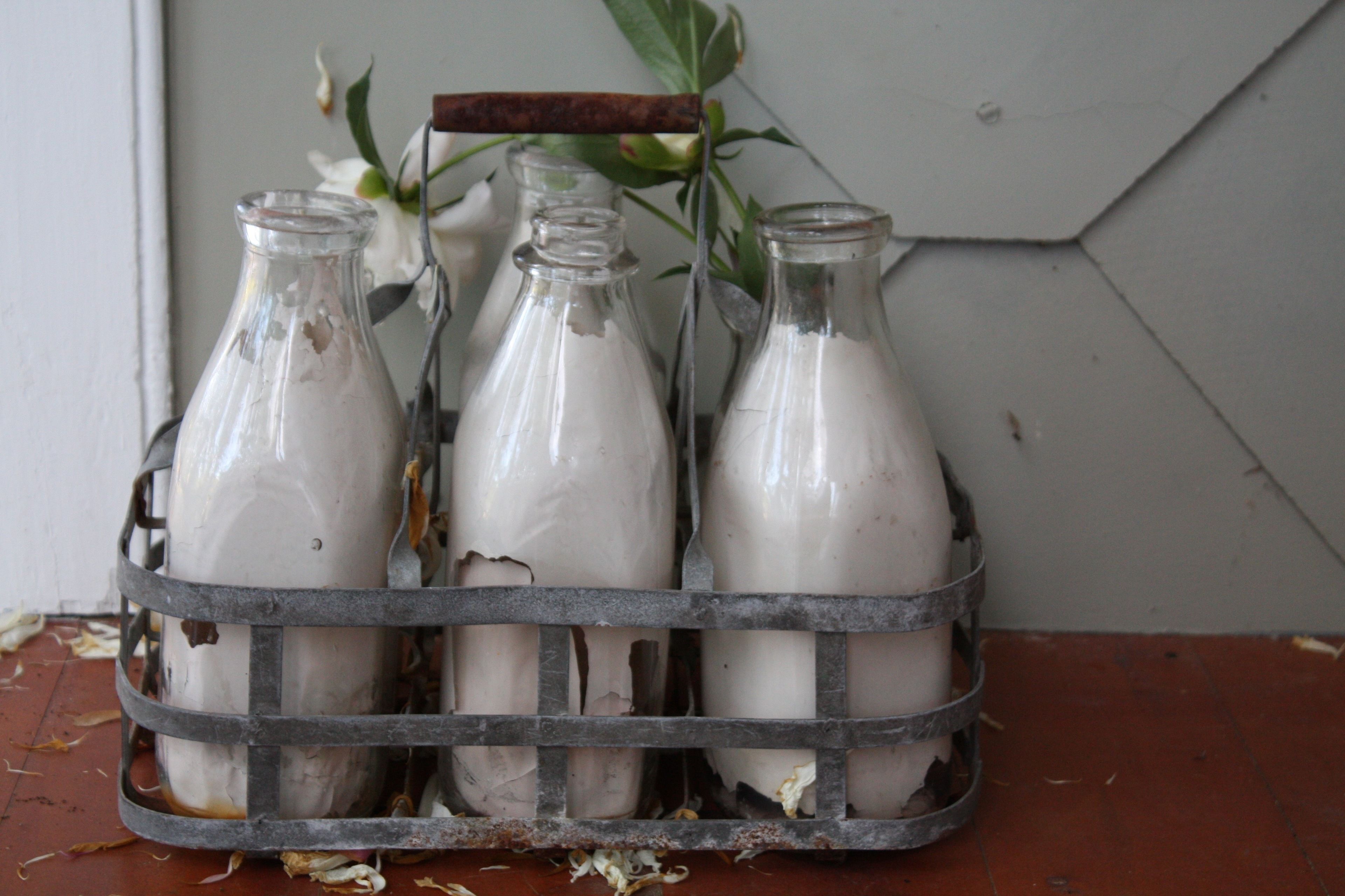 A metal crate holding four glass bottles with a wooden handle, placed on a tiled floor.