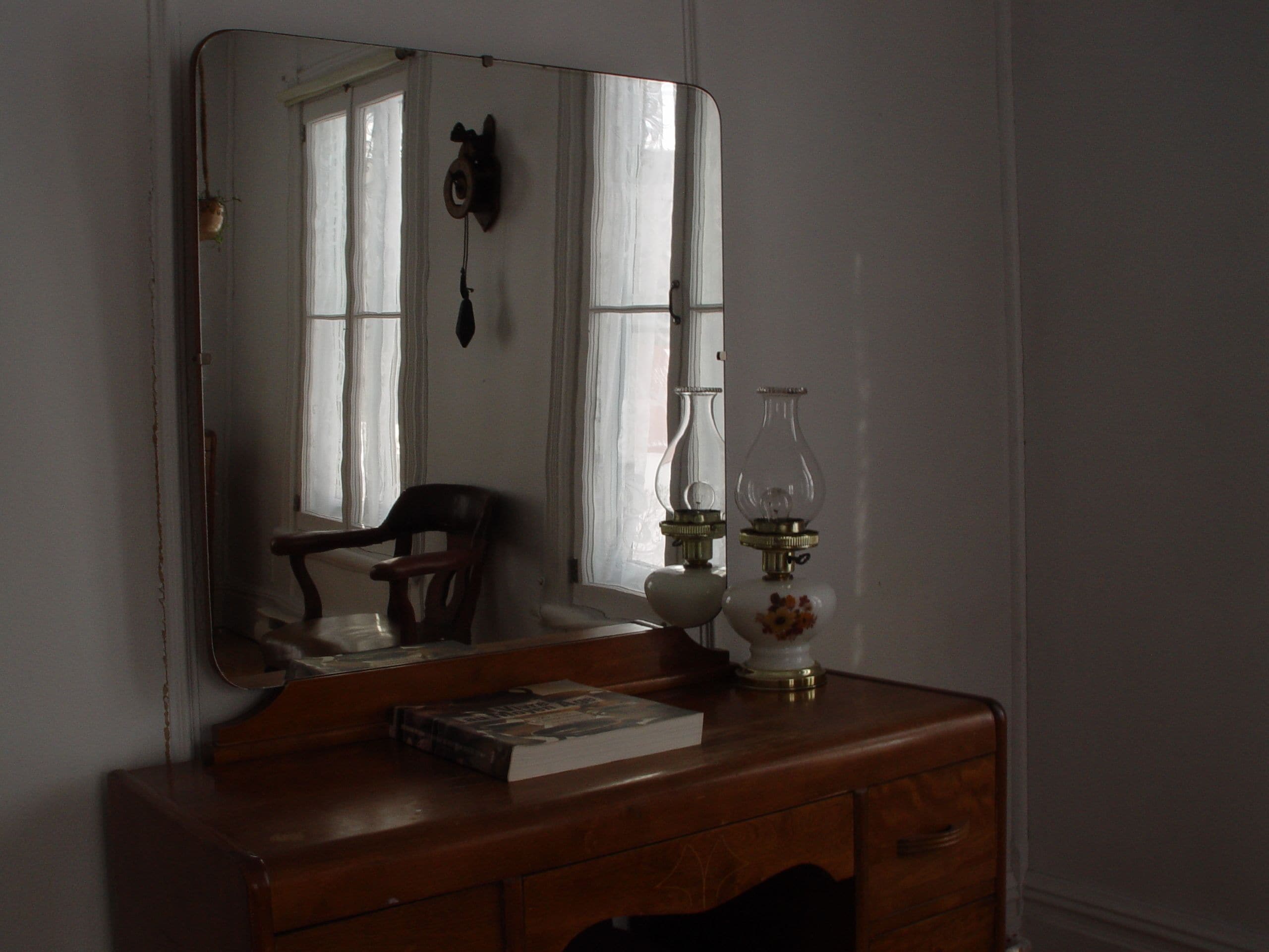 Une commode en bois avec un miroir, un livre et deux lampes en verre.