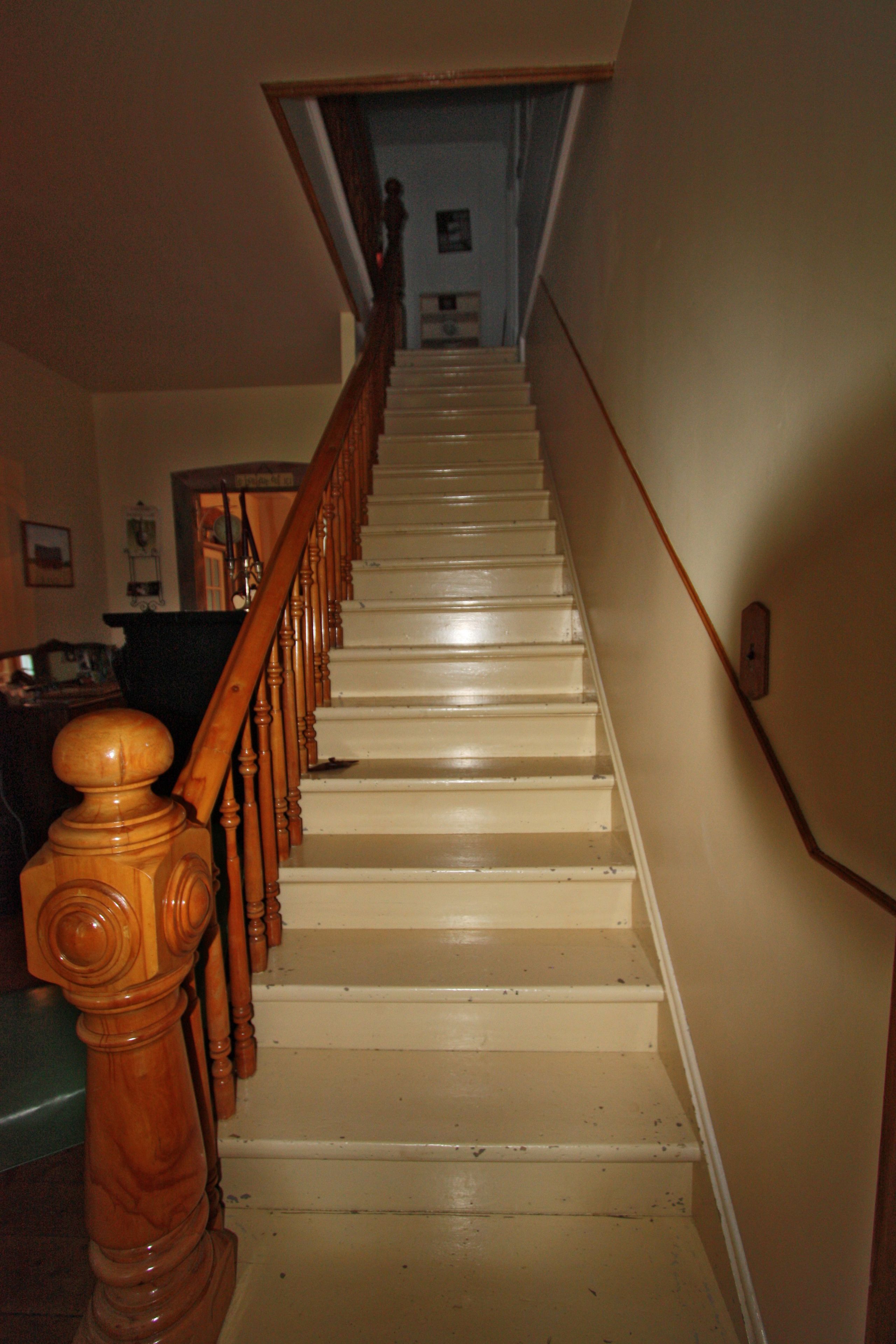 Una scala in legno con gradini bianchi e una ringhiera in legno che conduce a un piano superiore.