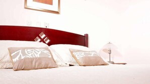 Una cama bien hecha con ropa de cama blanca y almohadas estampadas, un cabecero de madera y una lámpara de noche.