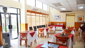 Un restaurante con varias mesas y sillas, un ventanal grande y una puerta.