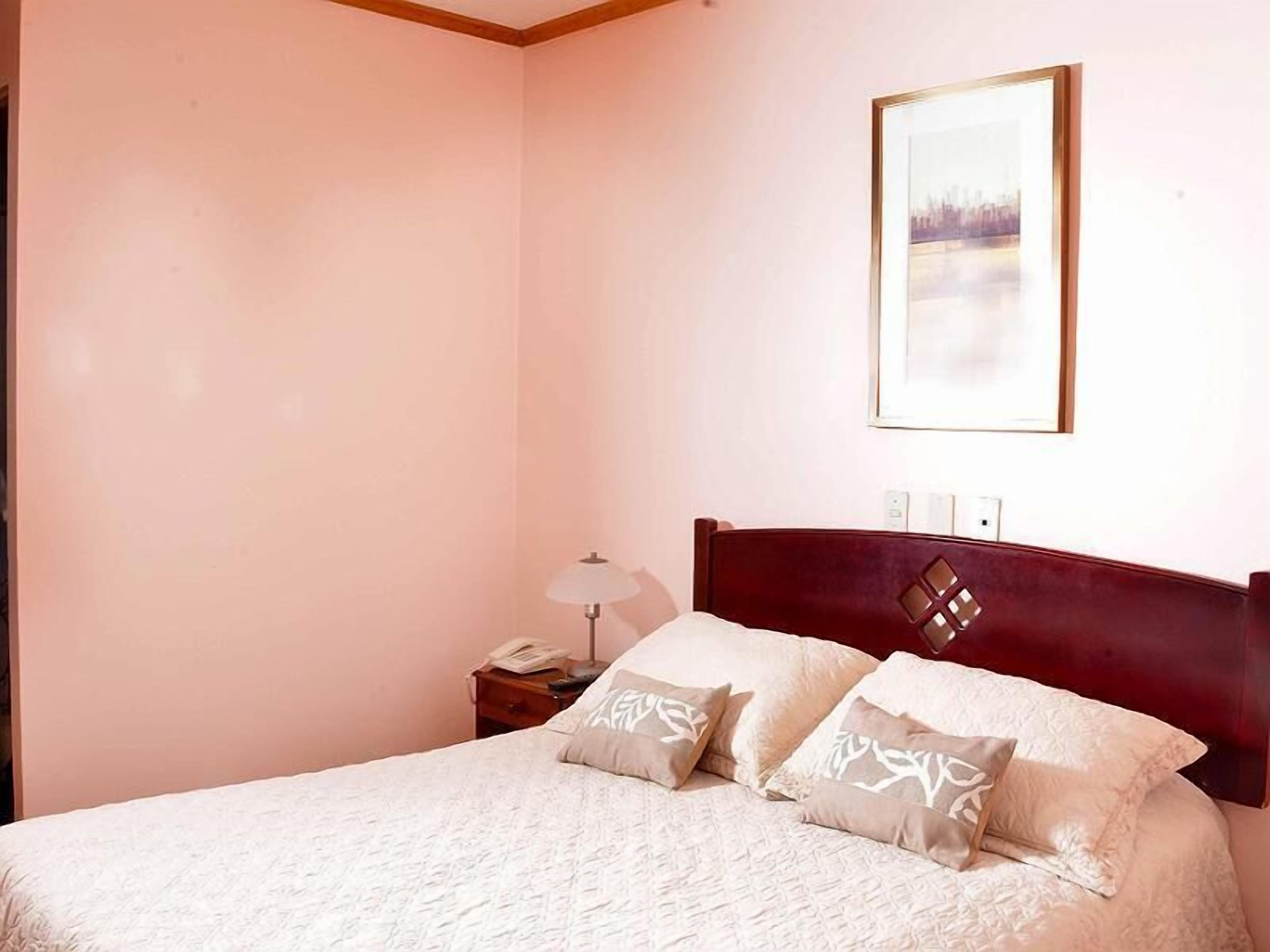 Un dormitorio con cama, mesita de noche, lámpara y un cuadro en la pared.
