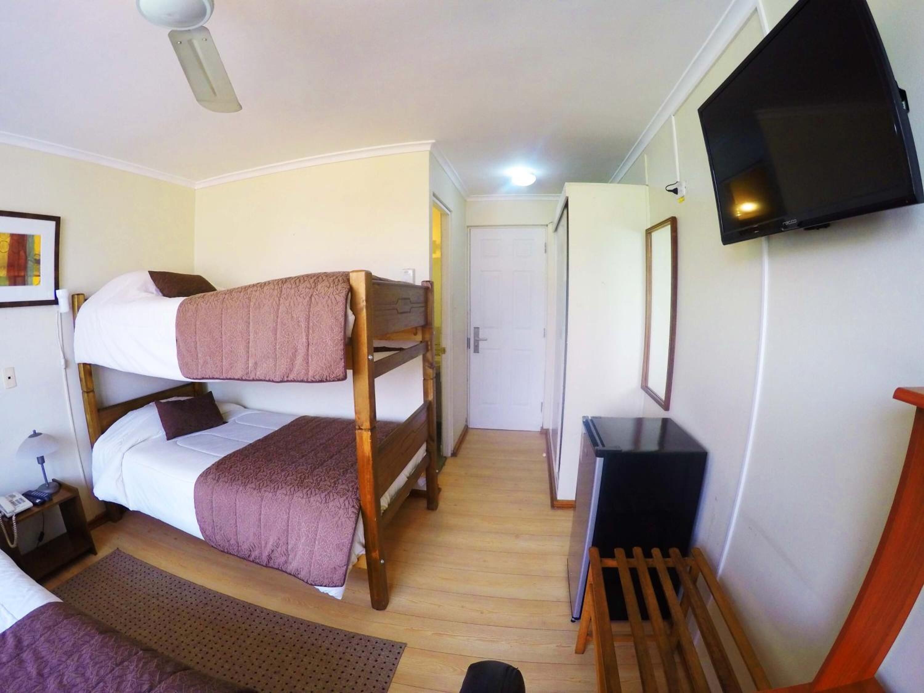 A room with bunk beds, a desk, a television, and a door leading to another room.