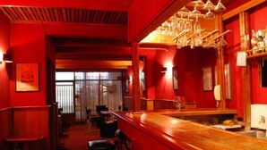 Zona de bar con mostrador de madera, taburetes y decoración roja.