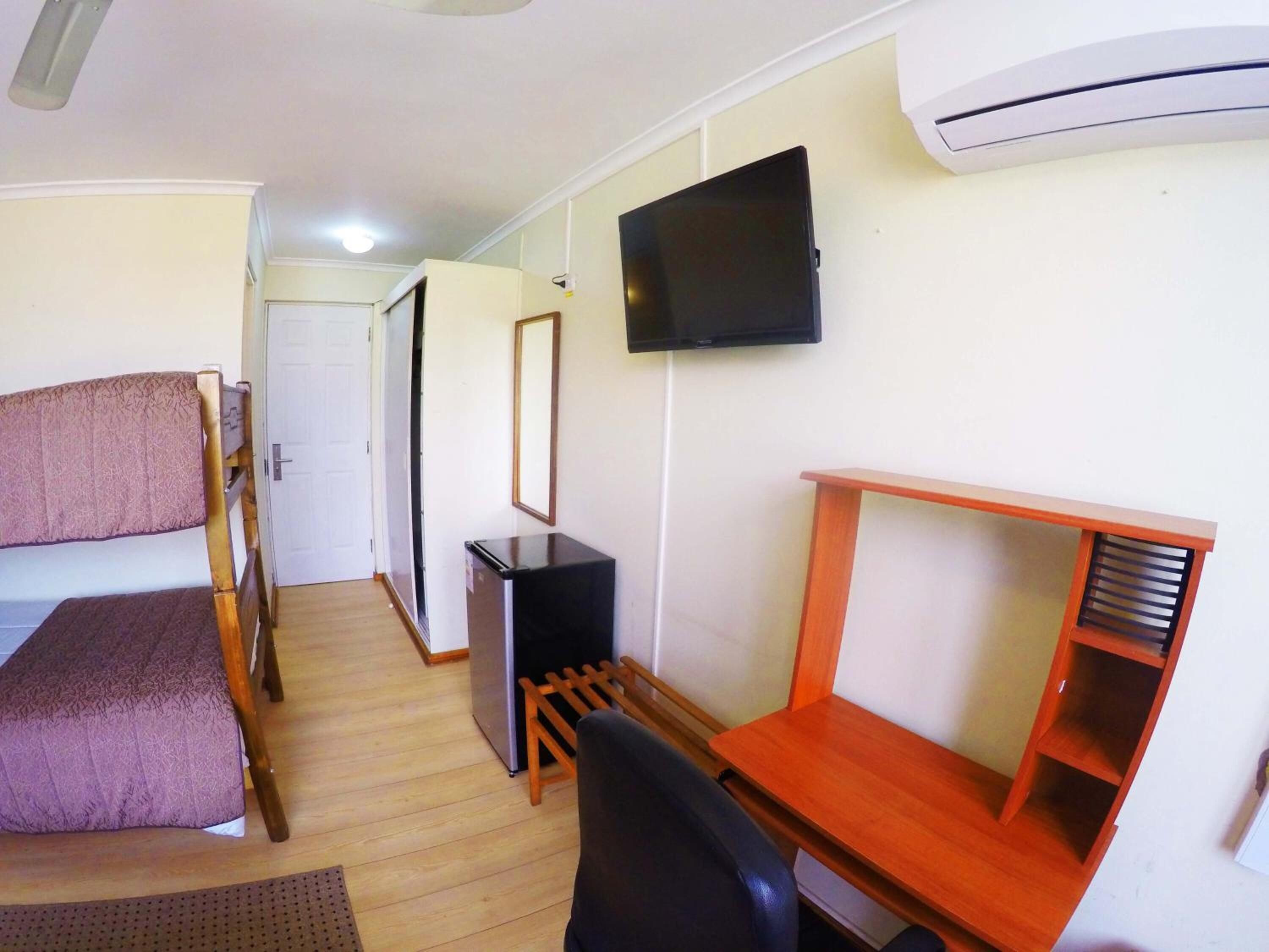 Una habitación con literas, un escritorio, una silla, un televisor y un aire acondicionado.