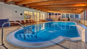 An indoor swimming pool with a wooden ceiling, clear glass walls, and sunlit windows. - Suite Hotel Binz Familienhotel Rügen (Binz)