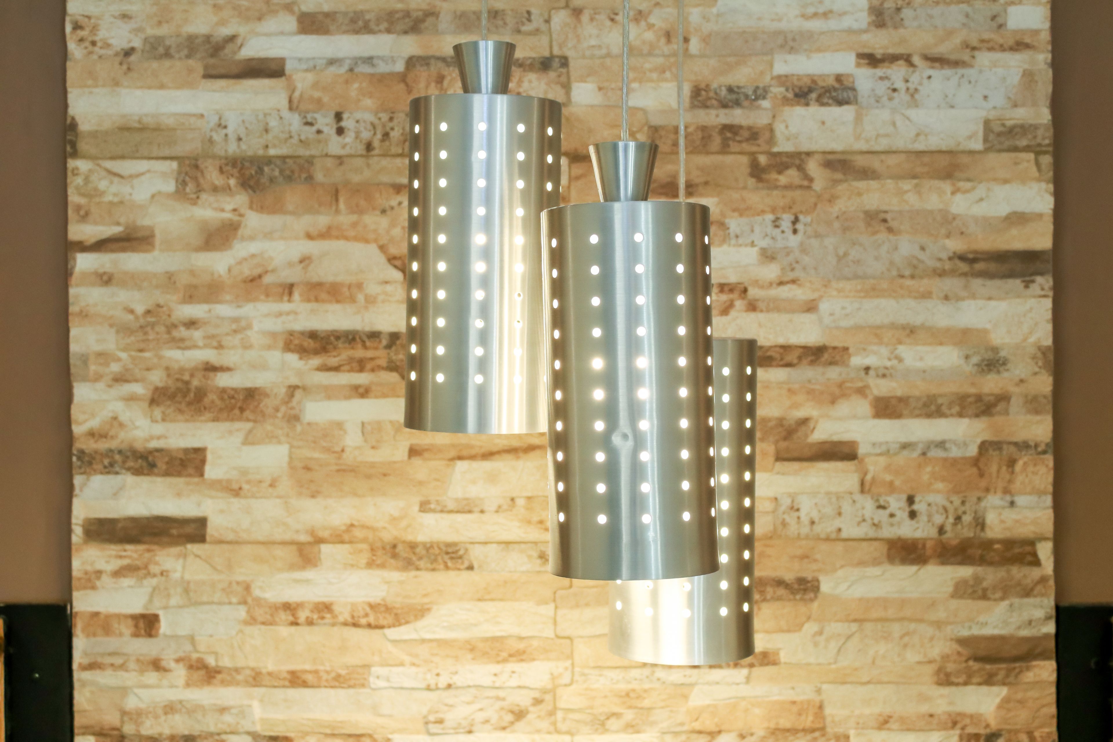 Un lustre moderne doté de plusieurs sources lumineuses, installé sur un mur en pierre à texture marquée.
