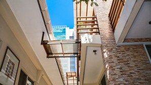 A narrow corridor with a wooden balcony and a view of a building with a blue sky. - Las Magnolias Hotel Boutique (San Salvador)