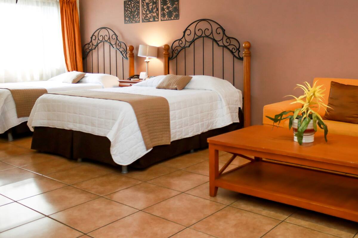 A hotel room with two beds, a sofa, a coffee table, and a lamp.