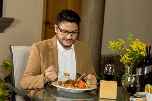 Une personne est assise à une table devant une assiette de nourriture, une bouteille de vin et un verre de vin.