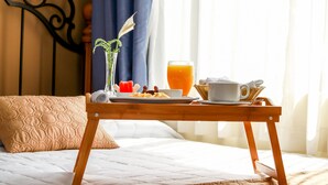 A neatly made bed with a wooden bedside table holding breakfast items, a vase with a plant, and a glass of orange juice. - Las Magnolias Hotel Boutique (San Salvador)