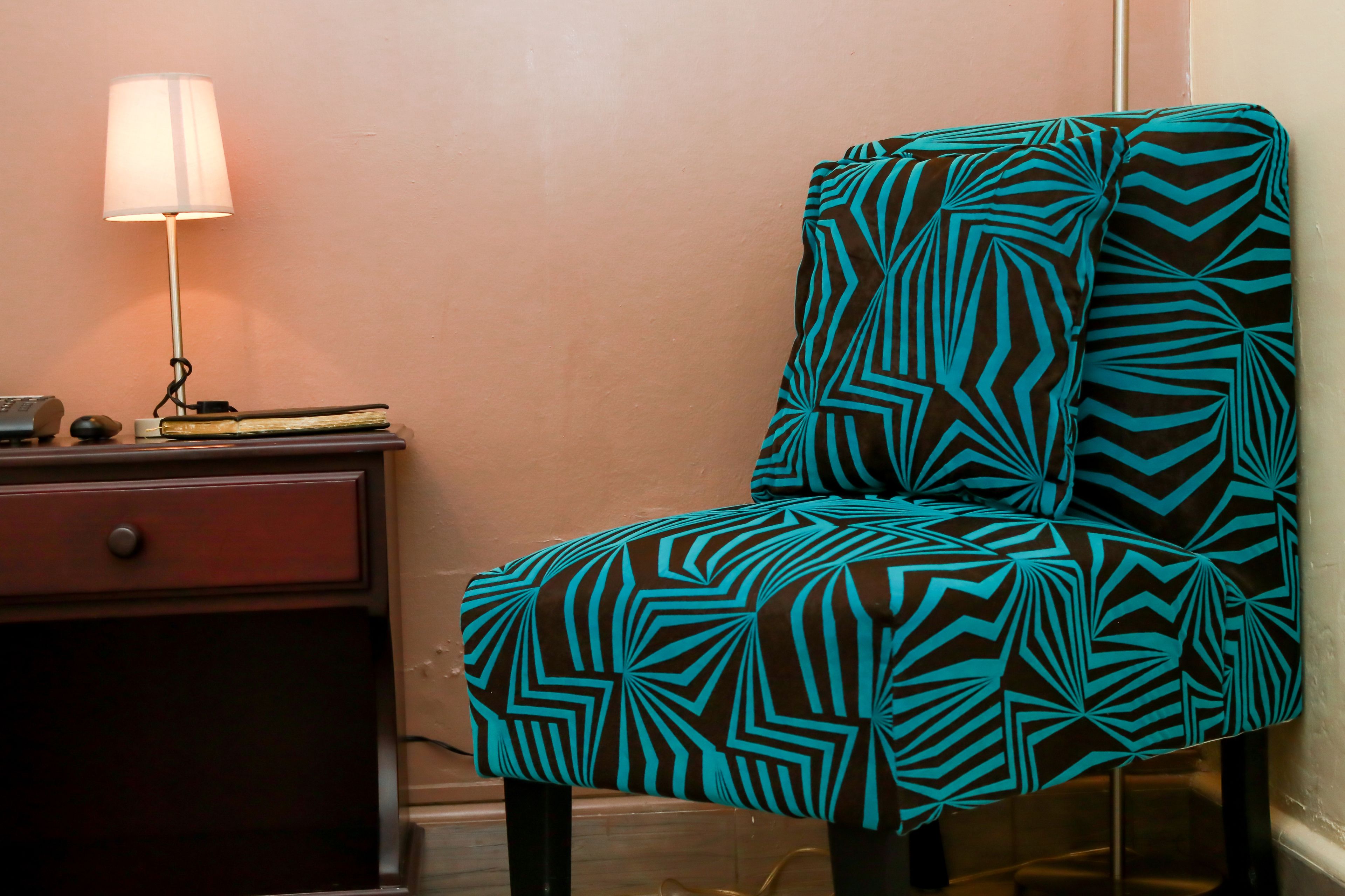 A chair with a geometric pattern, a lamp, and a small table with books.