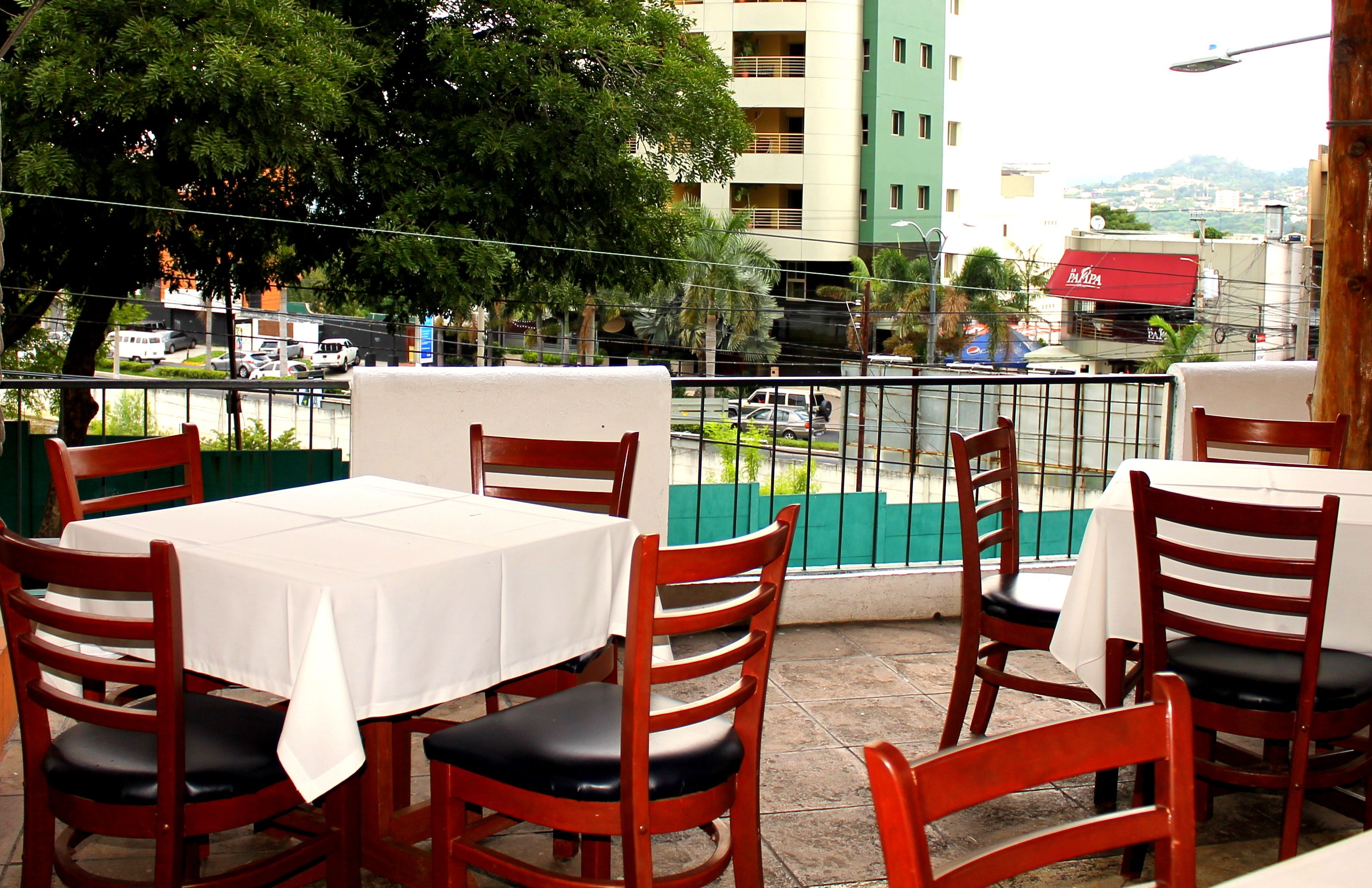 An outdoor dining area with tables and chairs, a view of a cityscape, and a building with a red awning in the background.
