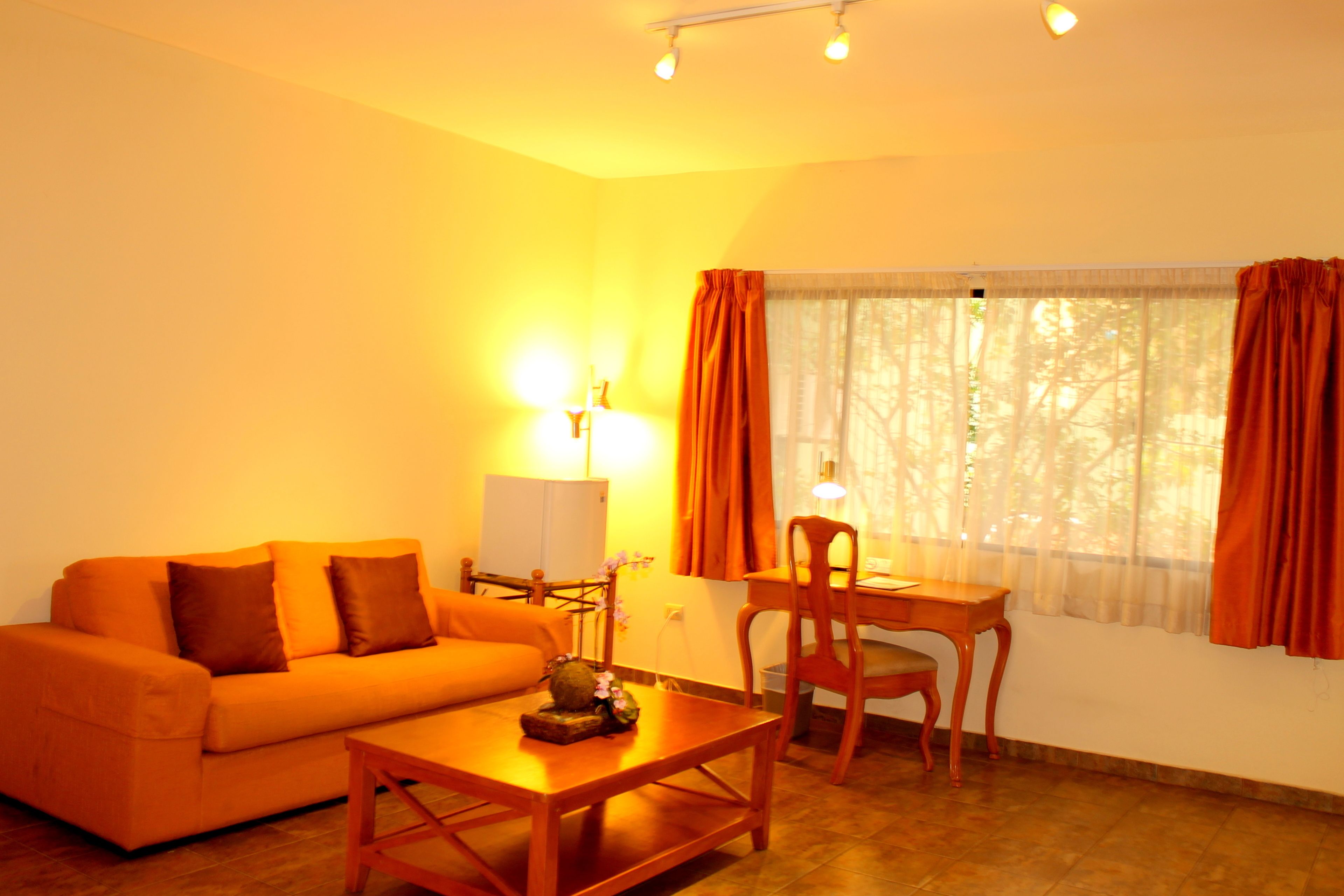 A living room with a sofa, a table, a lamp, and a chair. There is a window with curtains.