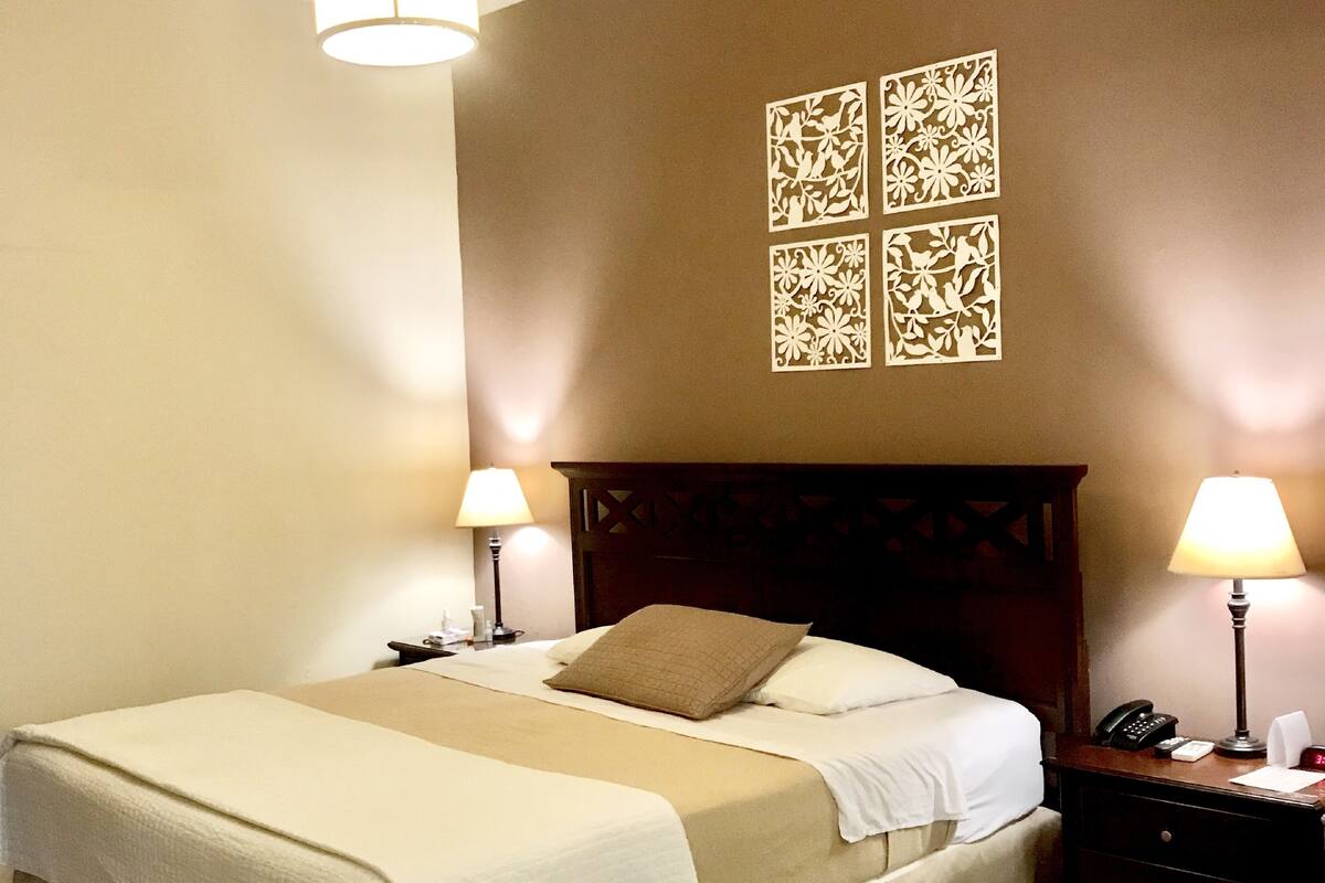 A neatly made bed with a headboard, two bedside lamps, and a wall with four square decorative panels.