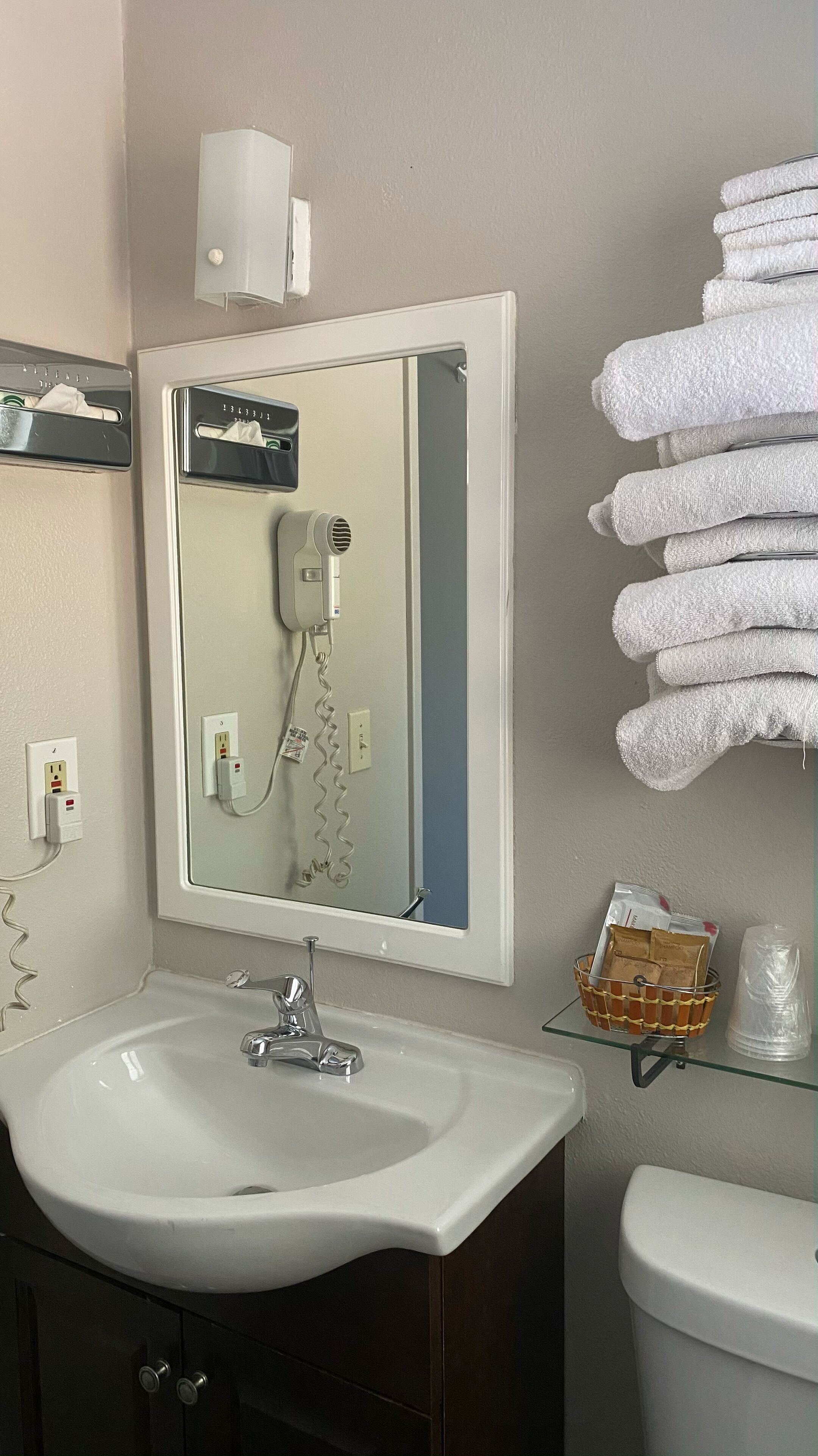 A bathroom with a white sink, a mirror, a hairdryer, and a stack of white towels.