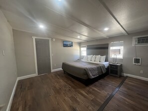 A bedroom with a bed, a nightstand, a painting, and a window. - Apex Inn (South Lake Tahoe)