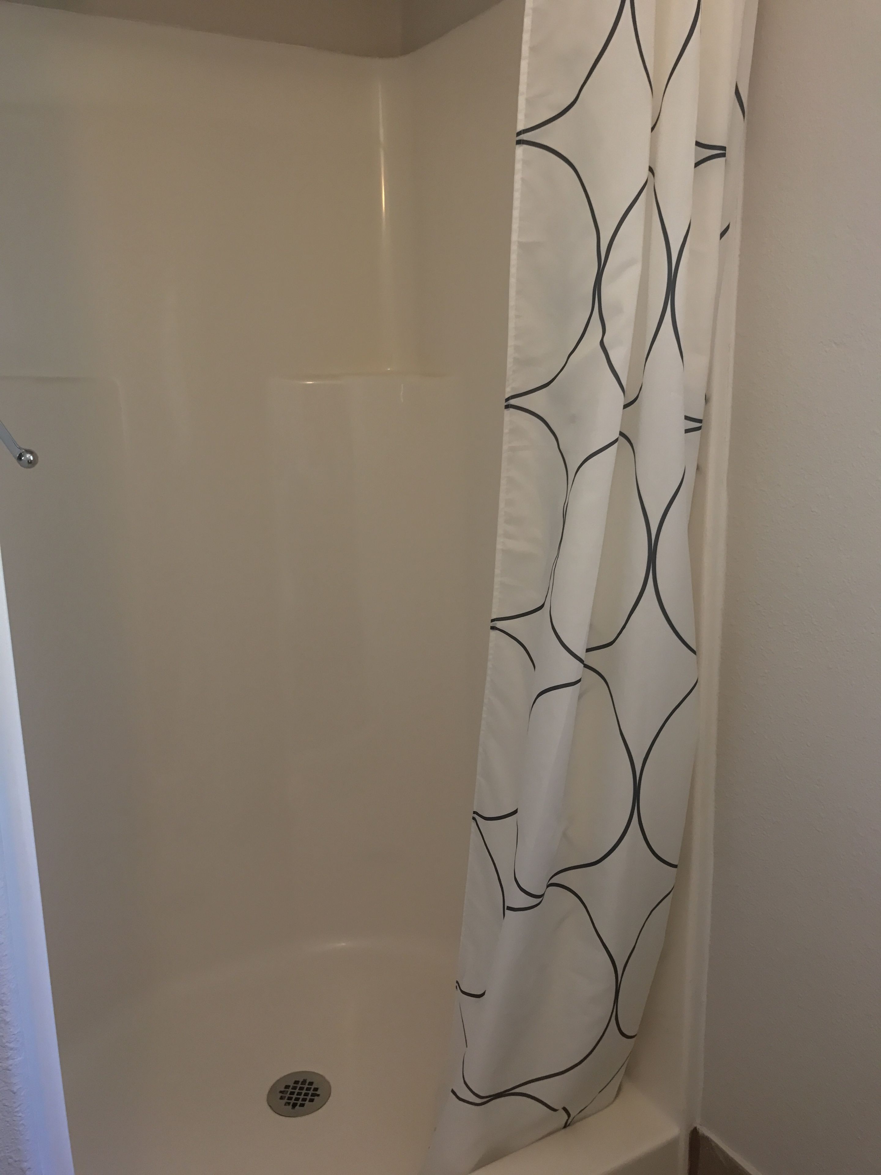 Une douche avec un mur blanc et un rideau orné d’un motif à rayures noires.