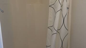 Une douche avec un mur blanc et un rideau orné d’un motif à rayures noires.