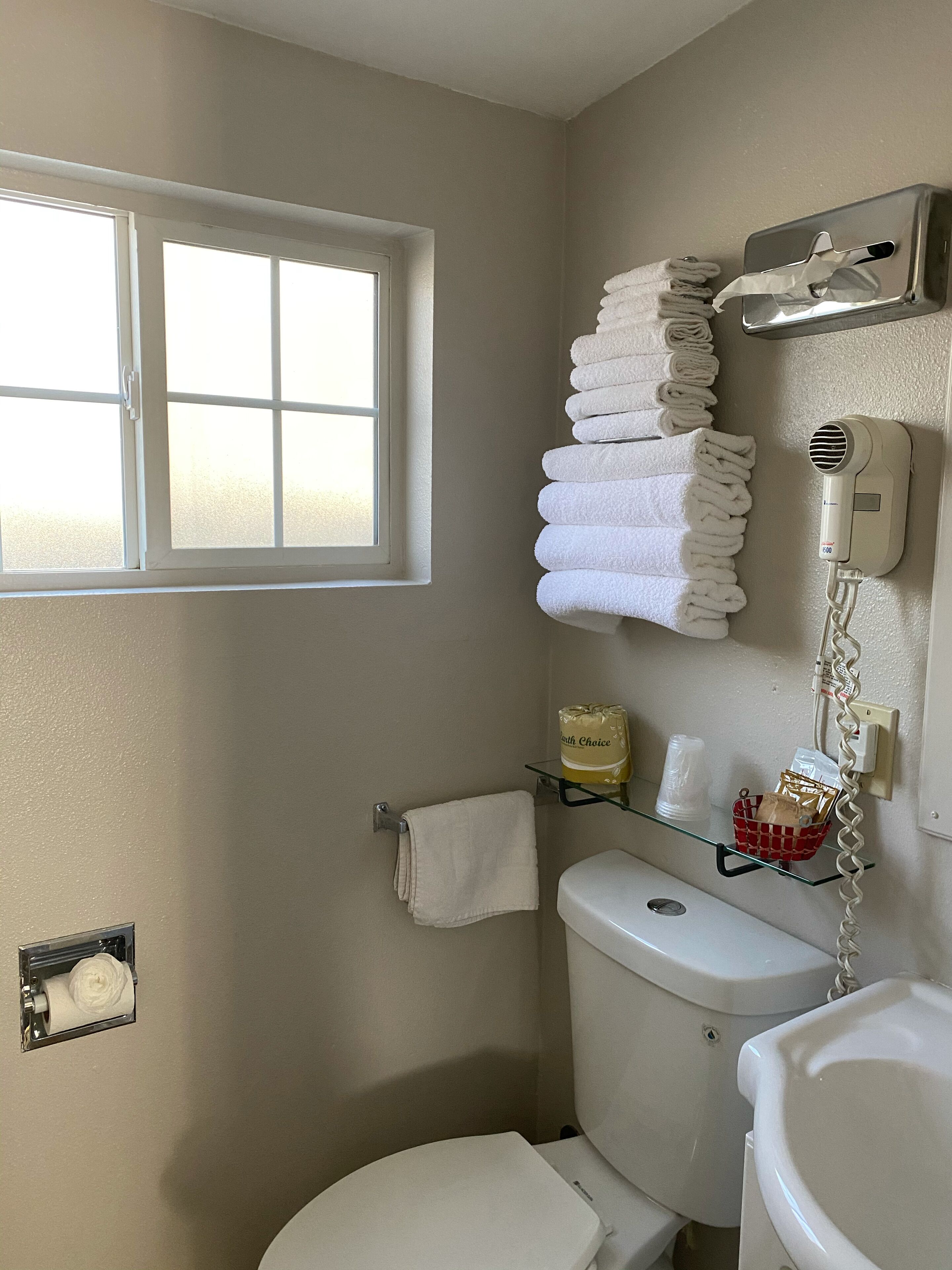 A bathroom with a toilet, a sink, a window, and a towel rack with neatly folded towels.