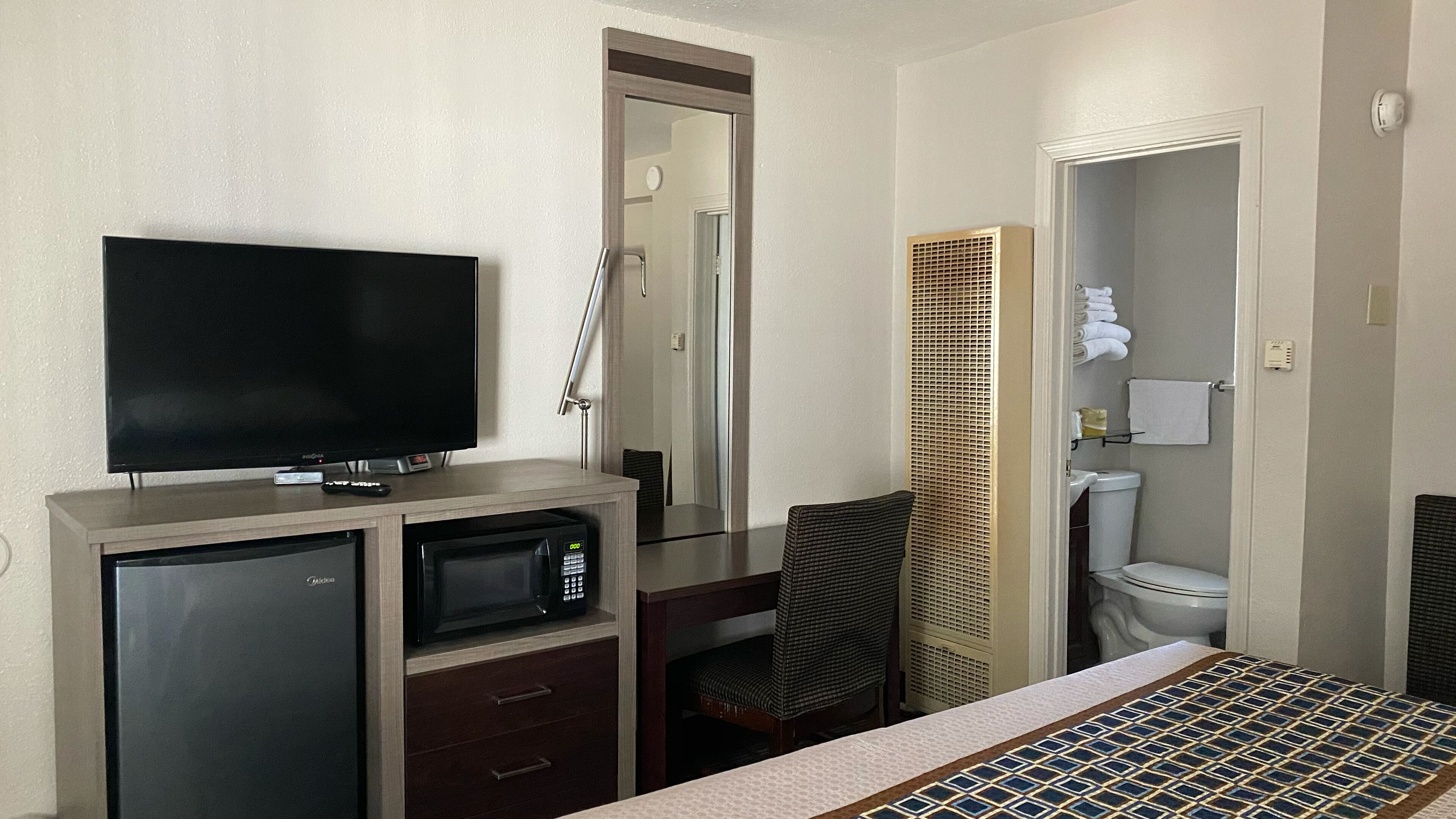 Une chambre d’hôtel équipée d’une télévision, d’un mini-réfrigérateur, d’un four à micro-ondes, d’un bureau, d’une chaise, ainsi que d’une salle de bain avec des toilettes et une douche.