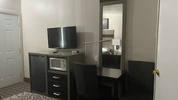 Una habitación de hotel con cama, escritorio, silla, televisor, microondas y espejo.