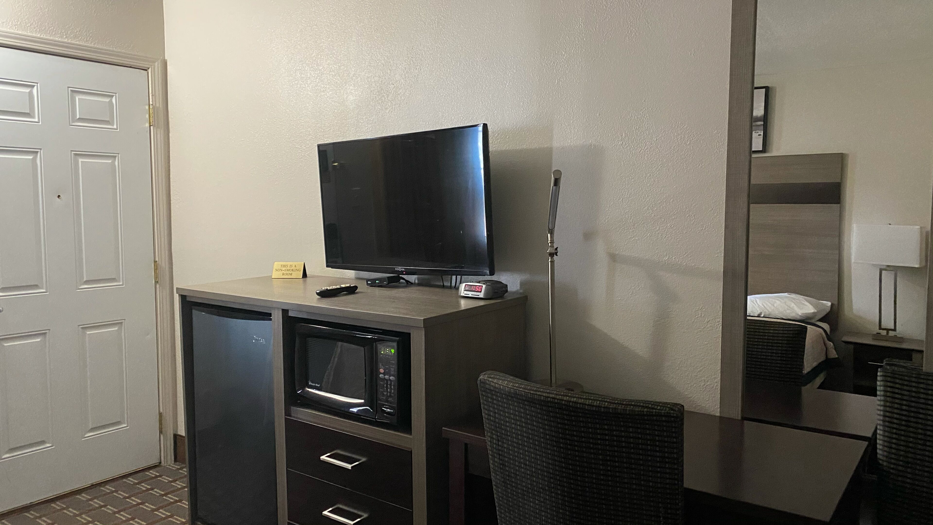 A compact hotel room with a television on a cabinet, a non-smoking sign, a microwave, and a small table with chairs.