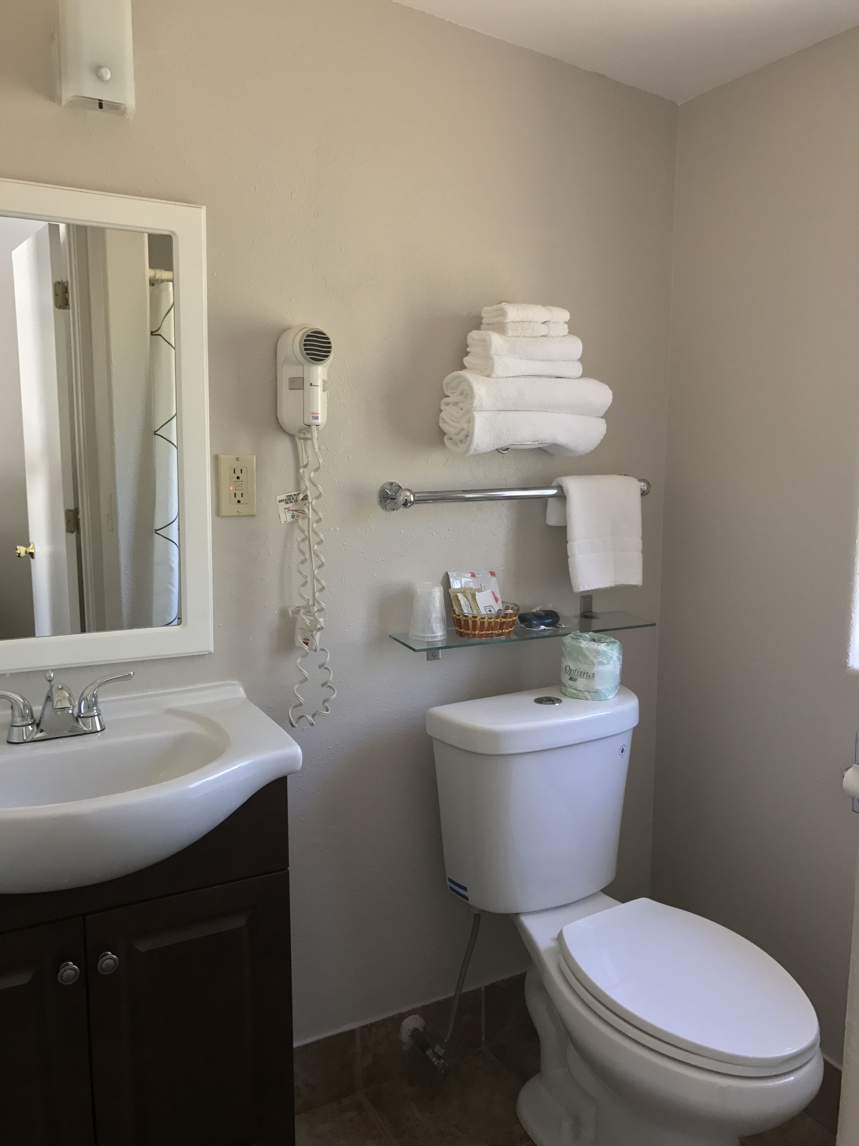 A bathroom with a white sink, a mirror, a hairdryer, a toilet, and a towel rack.