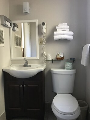 A bathroom with a white sink, dark cabinets, a toilet, a hand dryer, and a towel rack.