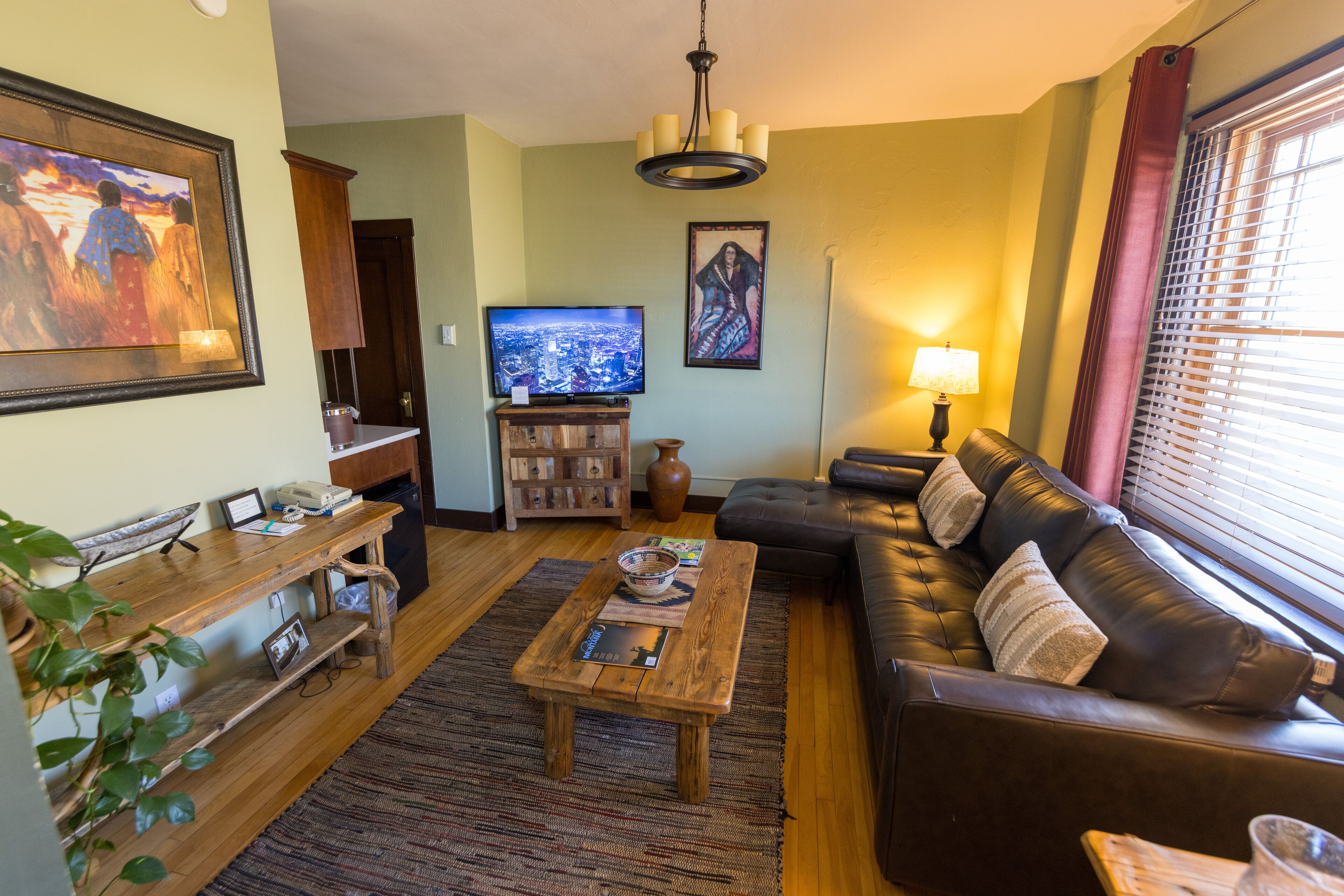 Een woonkamer met een houten salontafel, een leren bank, een televisie en een schilderij aan de muur.